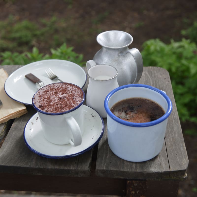 Zwei Emaillebecher mit Kaffee und Kakao auf einem Holztisch.
