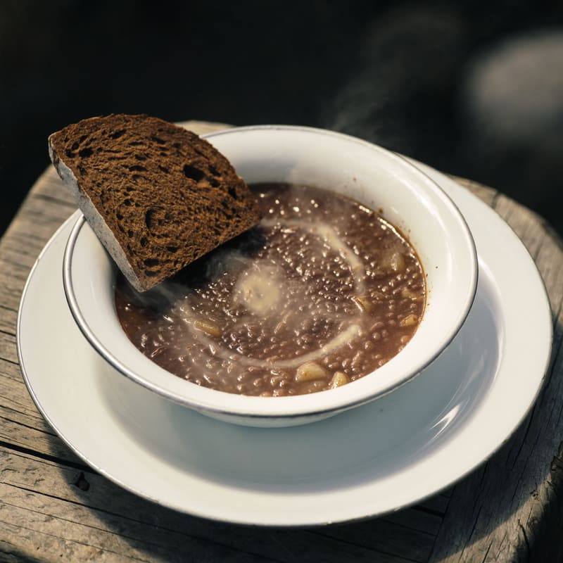 Schale Linsensuppe mit einer Scheibe Roggenbrot auf einem Holztisch.