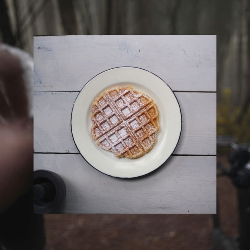 Frisch gebackene Waffel mit Puderzucker auf einem Emailleteller.